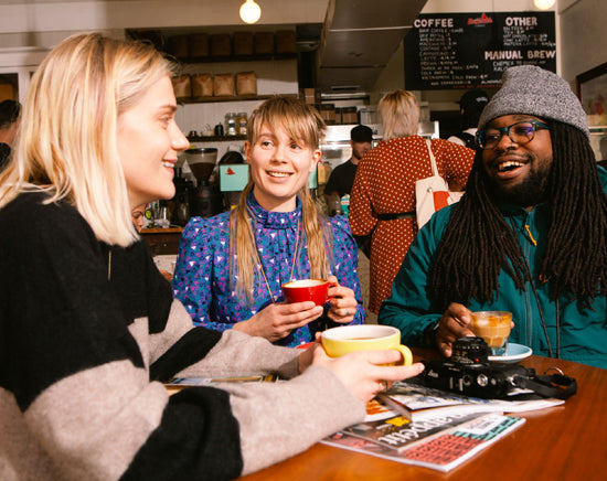 Three young people with coffee sitting having a conversation at Redhawk Coffee Roasters in Oakland with a Leica Camera.